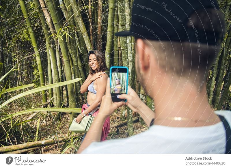 Crop tourist taking photo of cheerful girlfriend on smartphone woman take photo touch hair tourism bamboo using gadget smile device cellphone spend time weekend