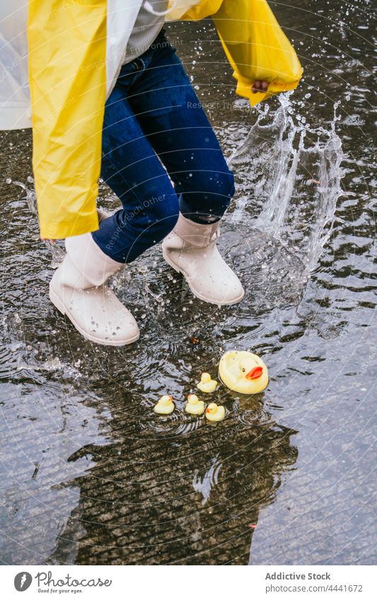 Crop girl in gumboots jumping on puddle with splashing water run having fun playful duck active energy reflection rainy childhood carefree spare time splatter