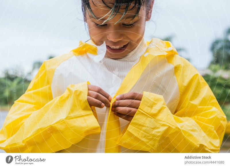 Crop smiling Asian girl buttoning up raincoat in park button up smile childhood friendly charming pleasant rainy weather cheerful content attentive sincere