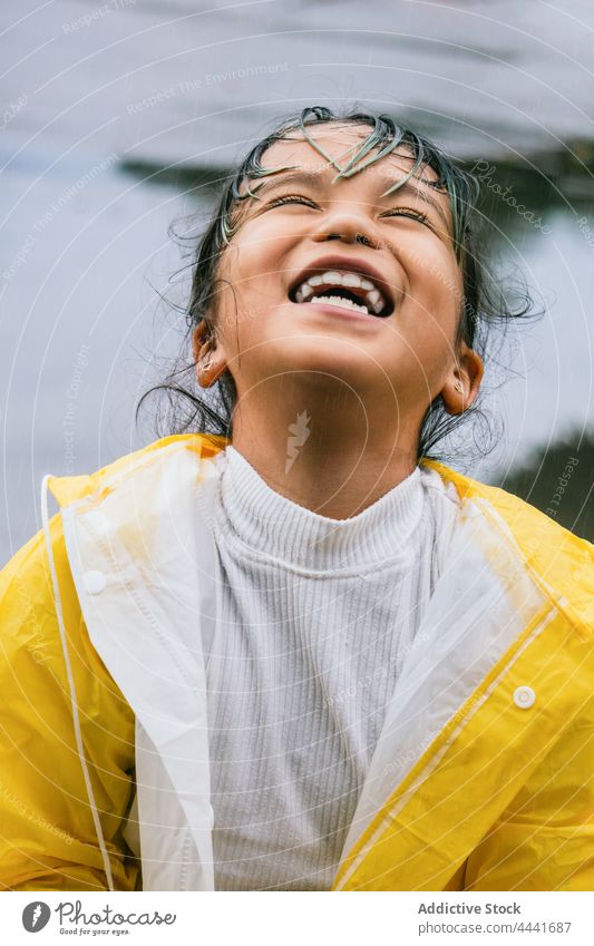 Cheerful ethnic girl in raincoat having fun in park cheerful play childhood carefree portrait spare time sky asian kid glad happy enjoy sincere content smile