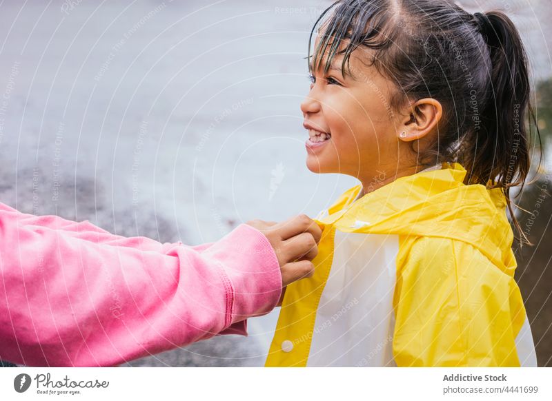 Crop mother buttoning up raincoat on smiling Asian daughter button up cheerful childhood interact spend time friendly rainy woman together girl carefree