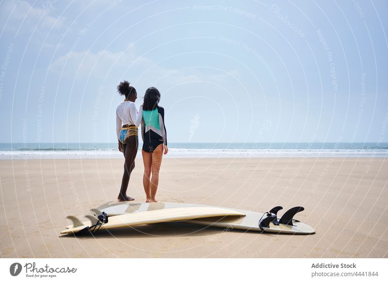 Smiling multiracial girlfriends with against surfboards on sea shore interact longboard sport ocean coast cheerful blue sky women sportswomen talk friendship