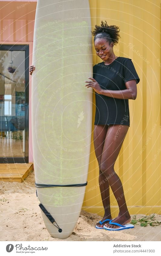 Smiling black surfer with longboard on shore smile sport surfing contemplate body woman coast beach cheerful ponder bikini t shirt wall sportswoman ethnic
