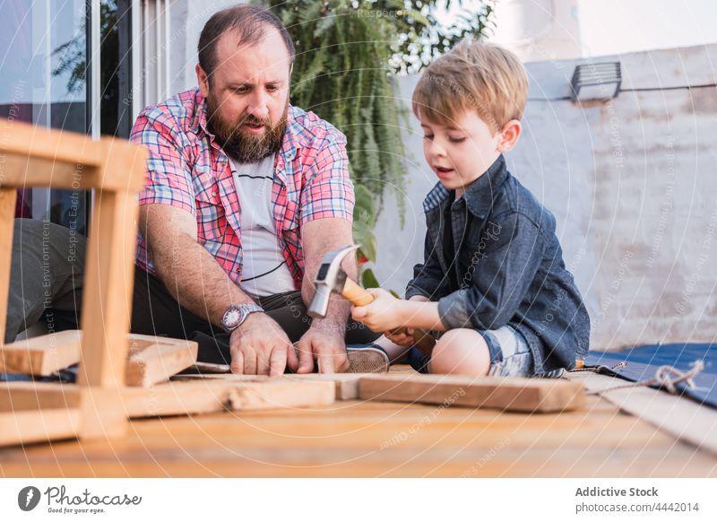 Father explaining to boy how to work with wood dad son woodwork show hammer handwork diy handicraft attentive man spend time talk point indicate speak hipster