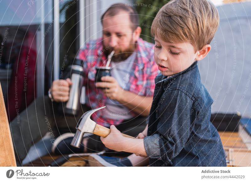Father drinking mate against son working with wood father thermos woodwork lumber attentive hammer pour diy break man dad herbal tea infused calabash gourd