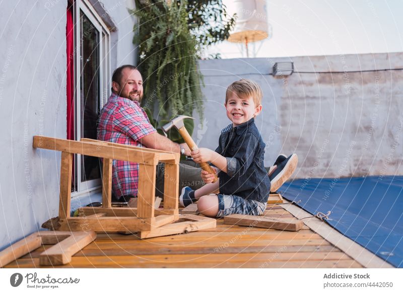 Father teaching boy how to work with wood dad son woodwork explain show hammer cheerful handwork diy glad handicraft attentive smile delight man spend time talk