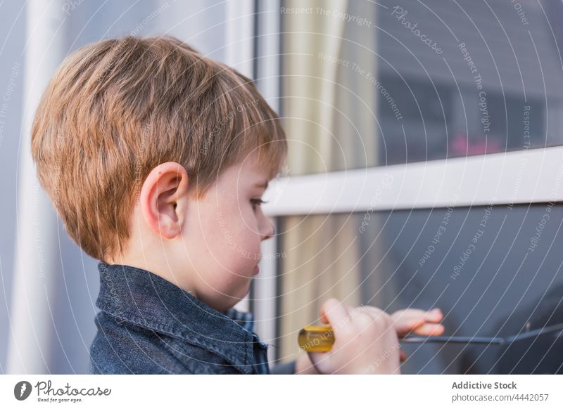 Attentive boy with manual screwdriver against window tool focus childhood free time instrument reflection attentive interested explore charming kid denim