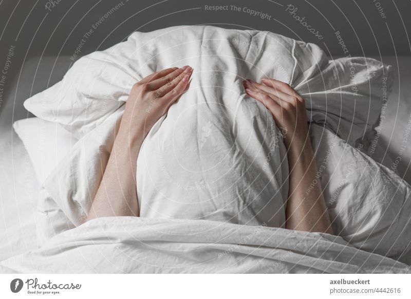 woman in bed hiding face under pillow hide cover sleep tired late riser long sleeper late sleeper unrecognizable person frustration noise anxiety stress