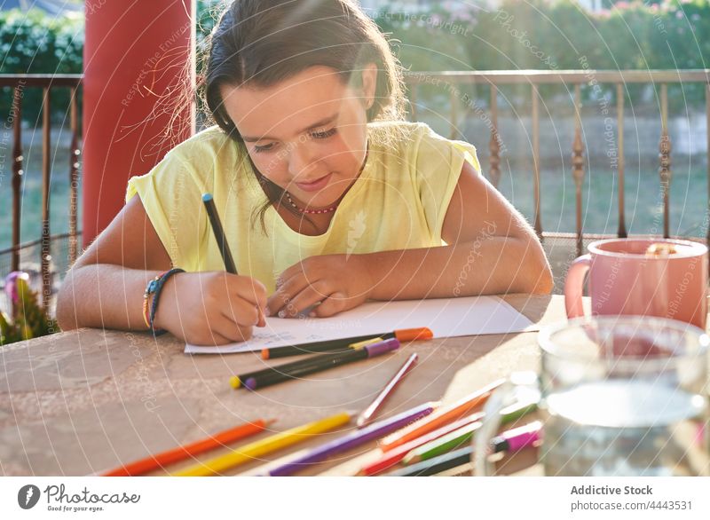 Focused girl drawing on paper on terrace in sunlight table kid creative positive hobby concentrate paint child casual childhood cheerful focus daylight colorful