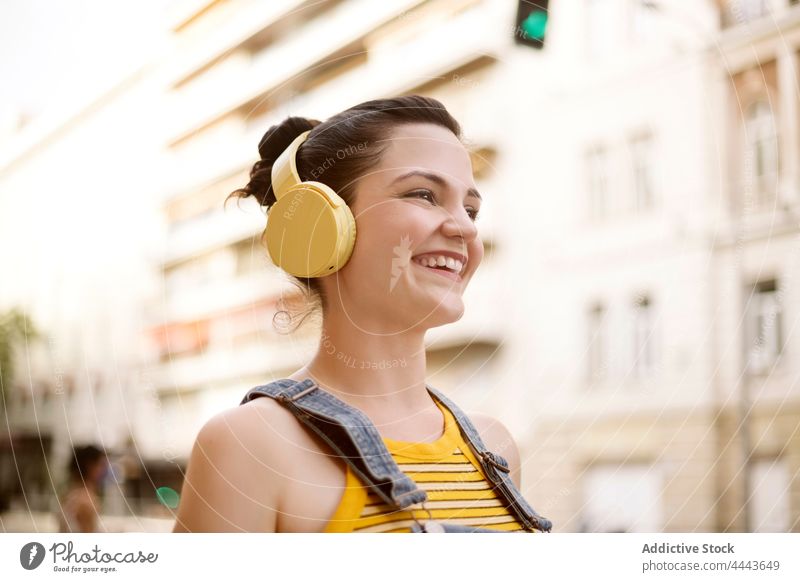 Cheerful woman in headphones walking on the street music listen wireless positive hobby enjoy carefree song female gadget delight audio millennial pleasure