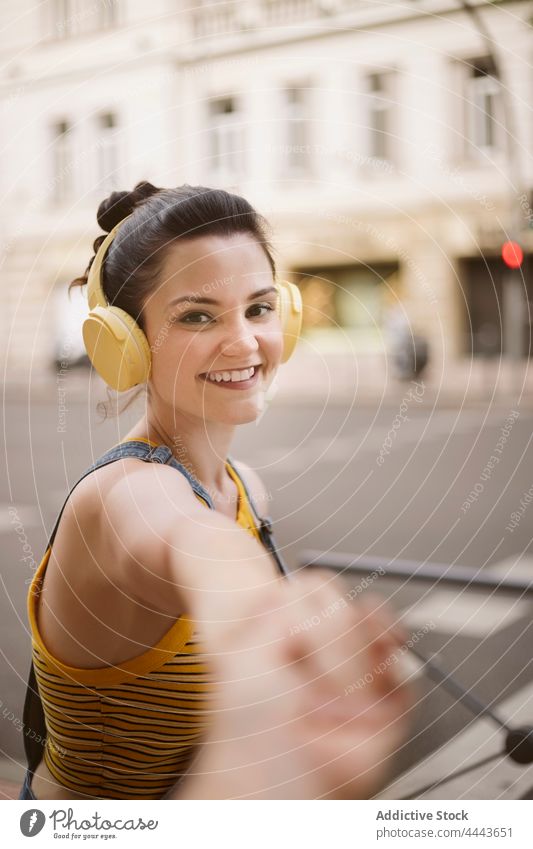 Cheerful woman in headphones reaching hand to camera music listen wireless positive hobby enjoy carefree song female gadget delight satisfied audio millennial