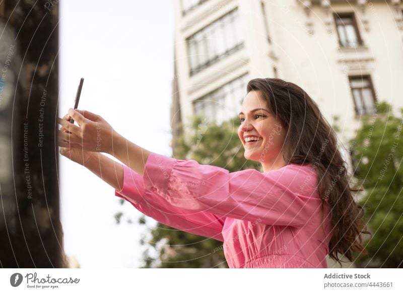 Anonymous woman taking selfie on smartphone on street smile take photo using connection online happy cheerful display digital city female delight mobile gadget