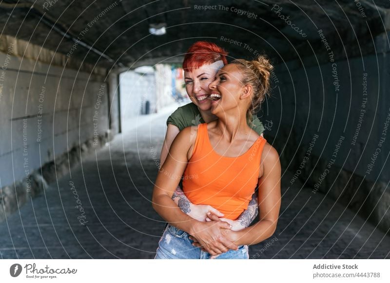 Happy lesbian couple embracing in urban tunnel embrace laugh relationship love romance interact cool women girlfriend romantic same sex trendy smile hug