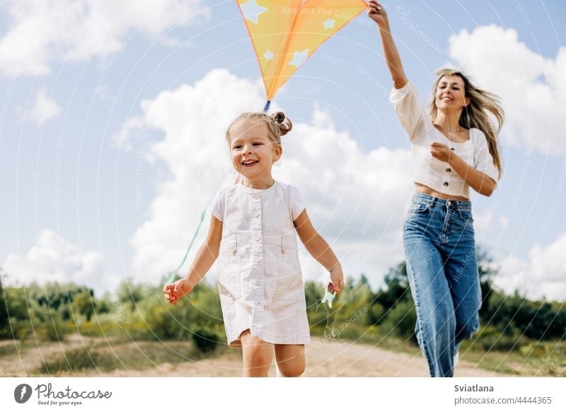 A laughing little girl and her mother run along the road to the field and fly a kite. Mom and daughter have fun together mom baby launching childhood playing