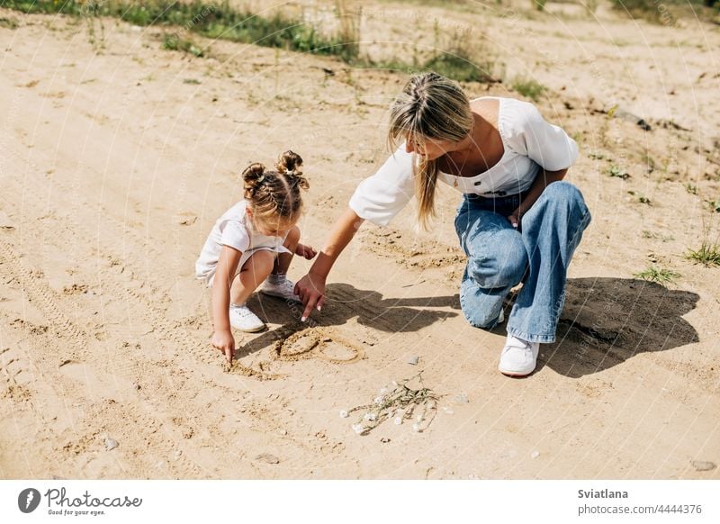 Mom and daughter draw together on the sand during a walk outside the city mother kid mom happy girl family drawing summer childhood woman young little love