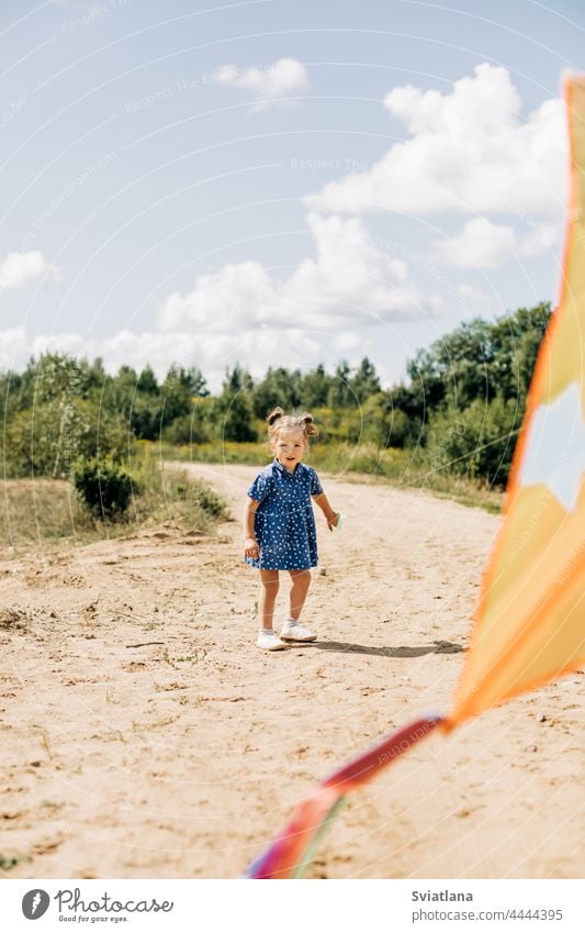 A little girl is flying a kite on a field road outside the city. Childhood, joy, care kid child summer outdoor fun person activity happy cute caucasian sunny