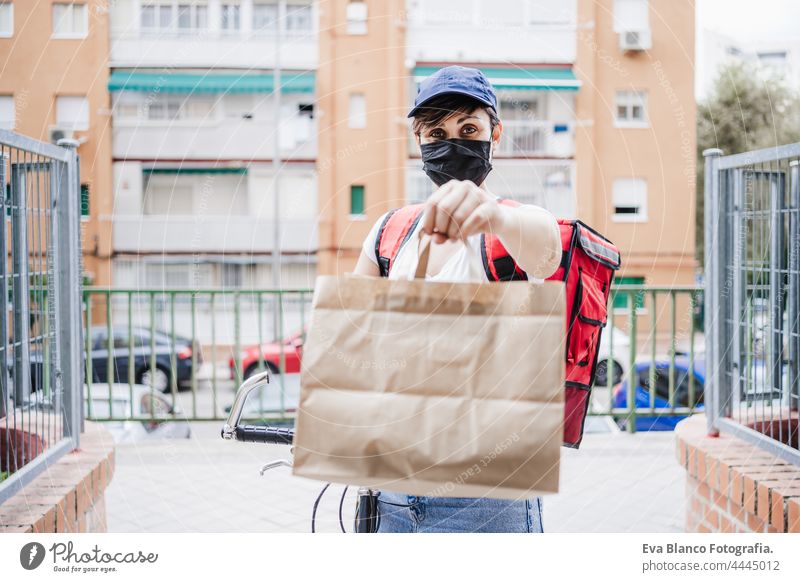 young woman rider delivering meal with bicycle while wearing mask for corona virus pandemic. Sustainable and healthy food concept face mask protective