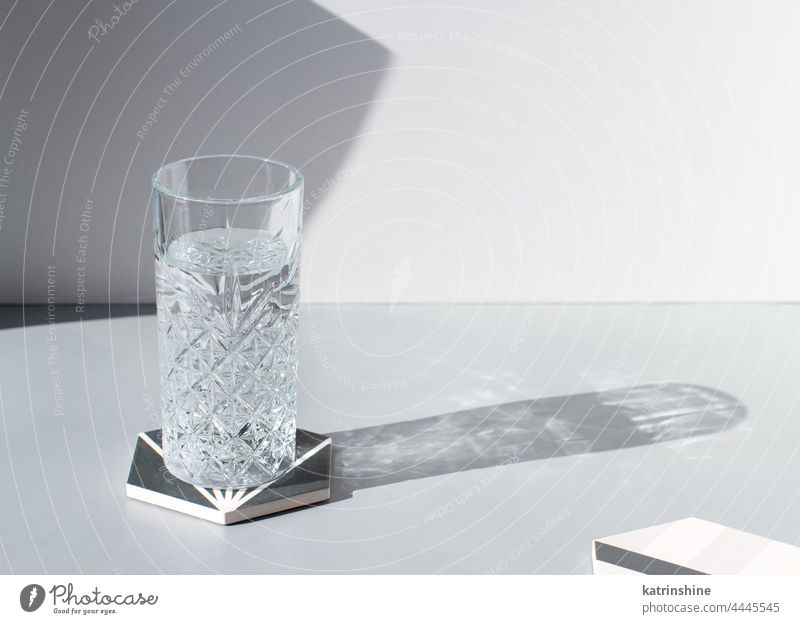 Faceted drinking glass of fresh clean water with shadow on grey table, copy space glassware hard light clear full summer aqua beverage cold cool crystal ecology