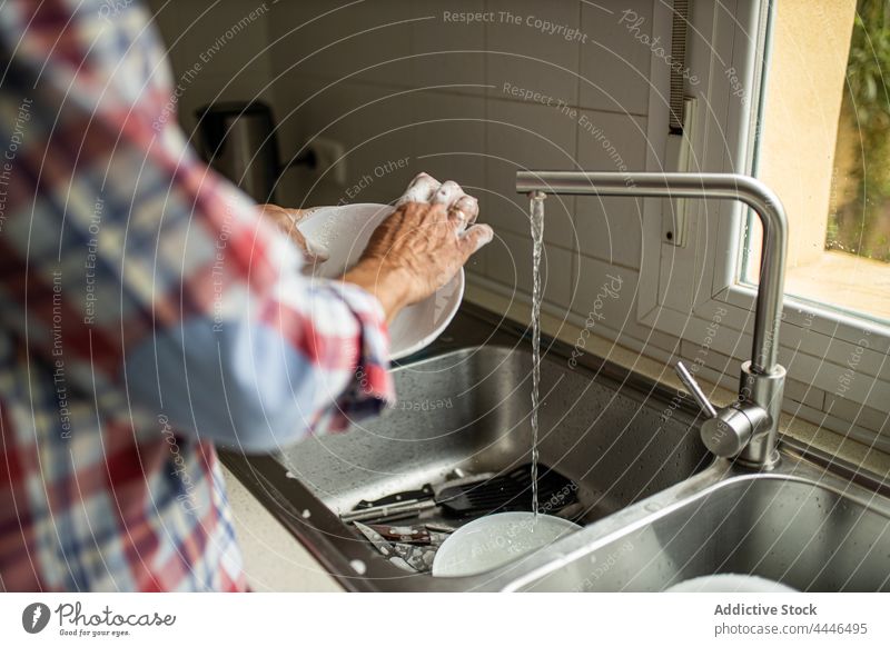 Anonymous man washing dishes in kitchen at home household cleanse window single stand leisure soap husband dishware kitchenware chore plate routine human