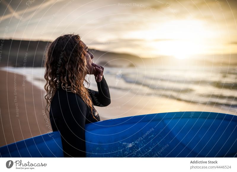 Woman standing whistling in the shore with surfboard looking at the sea during sunset woman sunrise wetsuit sportswoman fun whistle contemplate waves sunshine