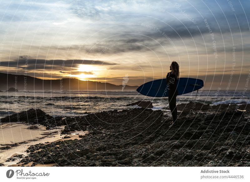 Woman standing in the shore with surfboard looking at the sea during sunset woman sunrise wetsuit sportswoman fun contemplate silhouette waves sunshine female