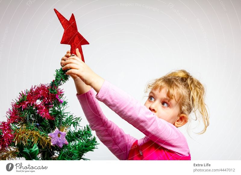 Child girl is arranging ornament decoration on artificial Christmas tree Adorable Arrange Artificial Assembly Blonde Caucasian Childhood Conifer Curve Cute