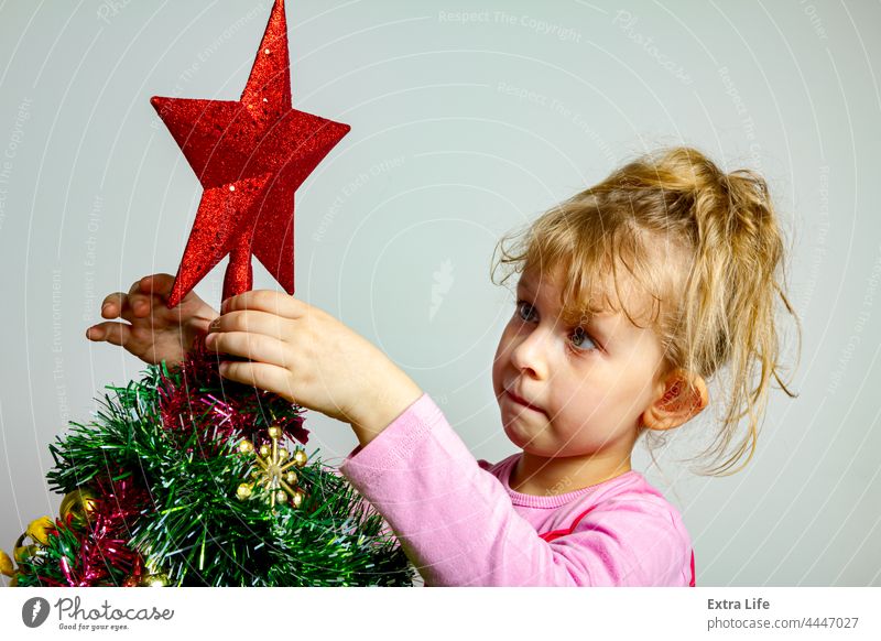 Child girl is arranging ornament decoration on artificial Christmas tree Adorable Arrange Artificial Assembly Blonde Caucasian Childhood Conifer Curve Cute