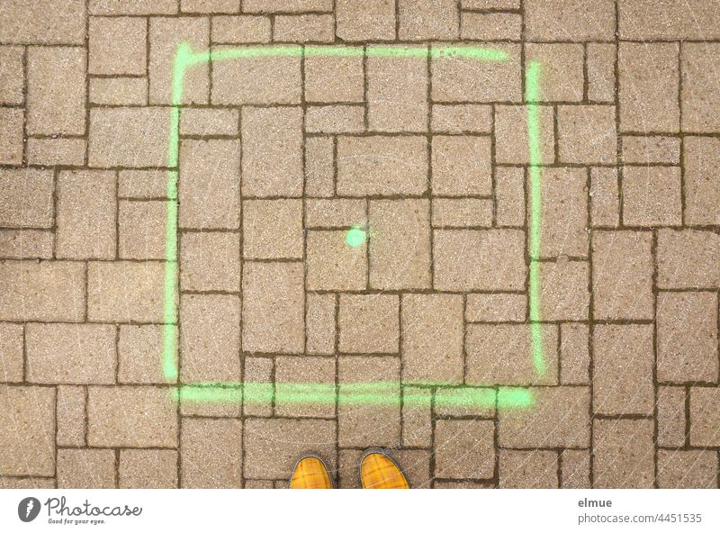 a square painted with green paint and a dot on a paved surface and yellow shoe tips in plan view / placeholder pavement paving Spot landing Paving stone