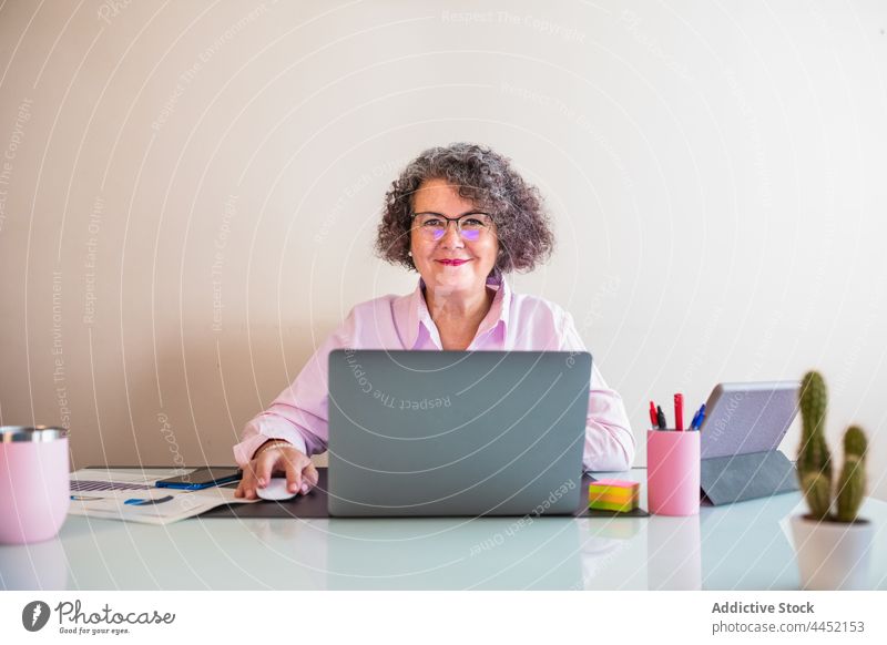 Smiling entrepreneur at desk with laptop in office smile independent confident internet woman using elderly gadget device cheerful businesswoman supply tablet