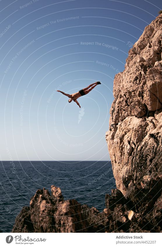 Sportsman jumping from rock into sea with horizon sportsman fly energy adrenalin extreme sky sporty outstretch trick active dynamic fearless leap barefoot