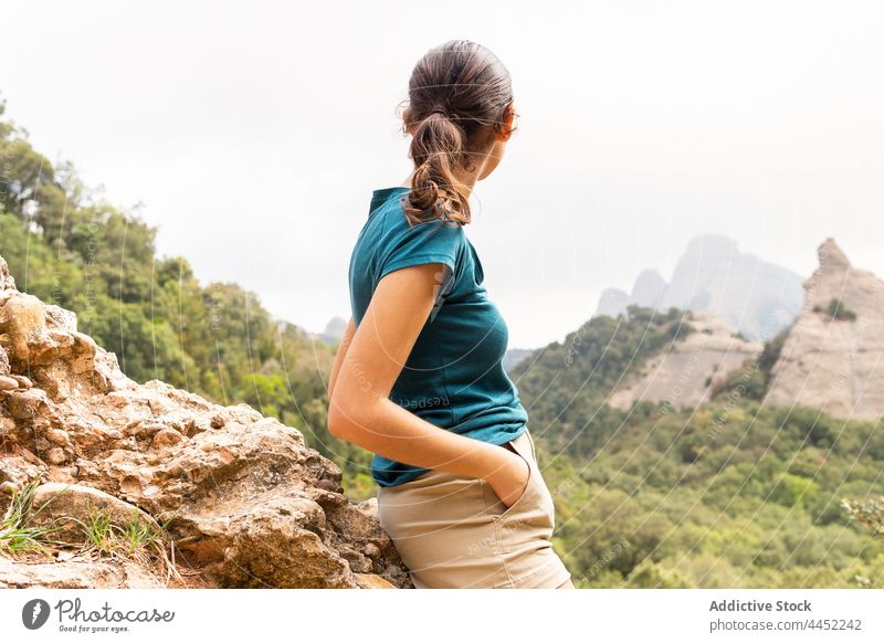 Smiling tourist admiring mount with green trees during trip traveler contemplate mountain montserrat nature highland hand on hip woman excursion admire lush
