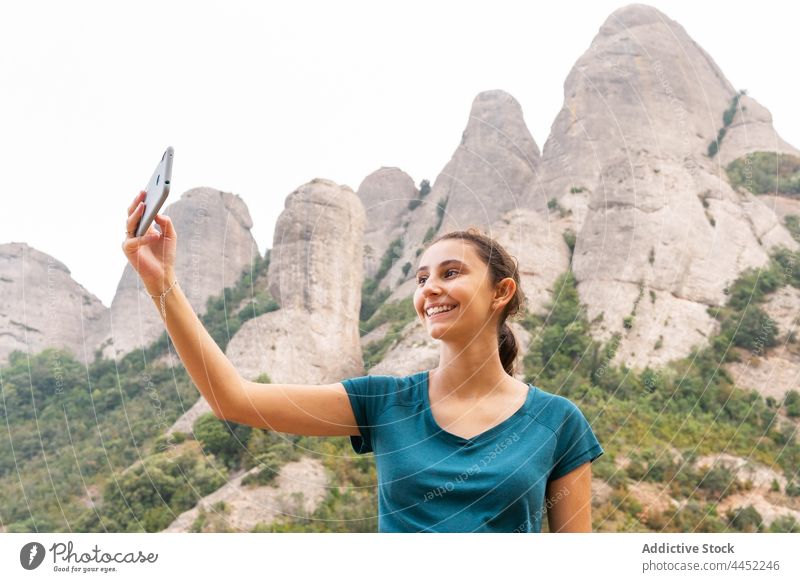 Smiling woman taking selfie on smartphone in rocky landscape tourist mountain range positive using highland trip female traveler self portrait sightseeing