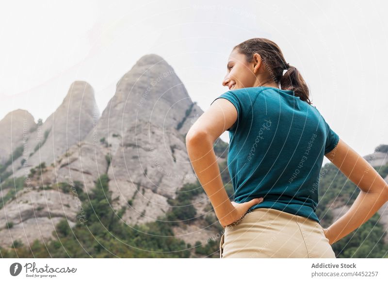 Smiling tourist admiring mount with green trees during trip traveler contemplate mountain montserrat nature highland smile hand on hip woman excursion admire