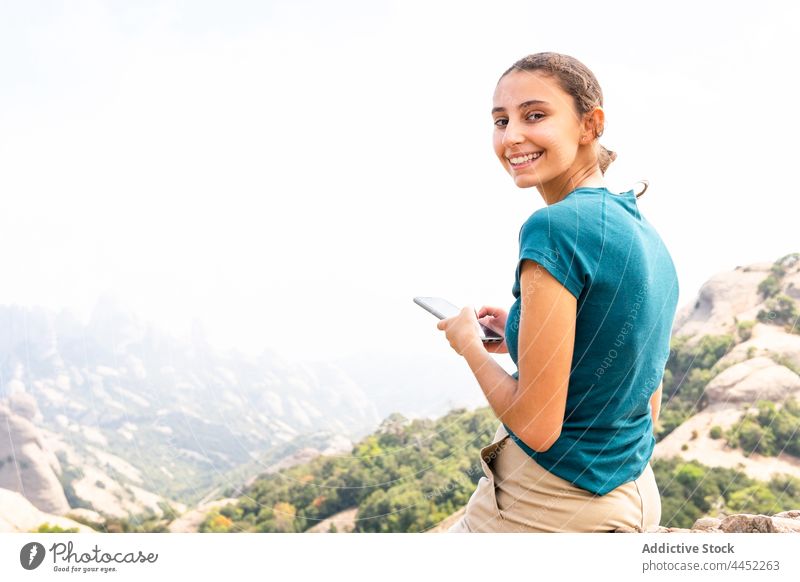 Smiling woman using smartphone during excursion in mountains tourist message highland explore positive rocky female travel vacation gadget device journey