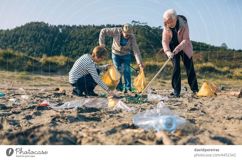Senior volunteers cleaning the beach senior group picking up trash rake picking up clip crouched dirty volunteering ecological conscience tools family