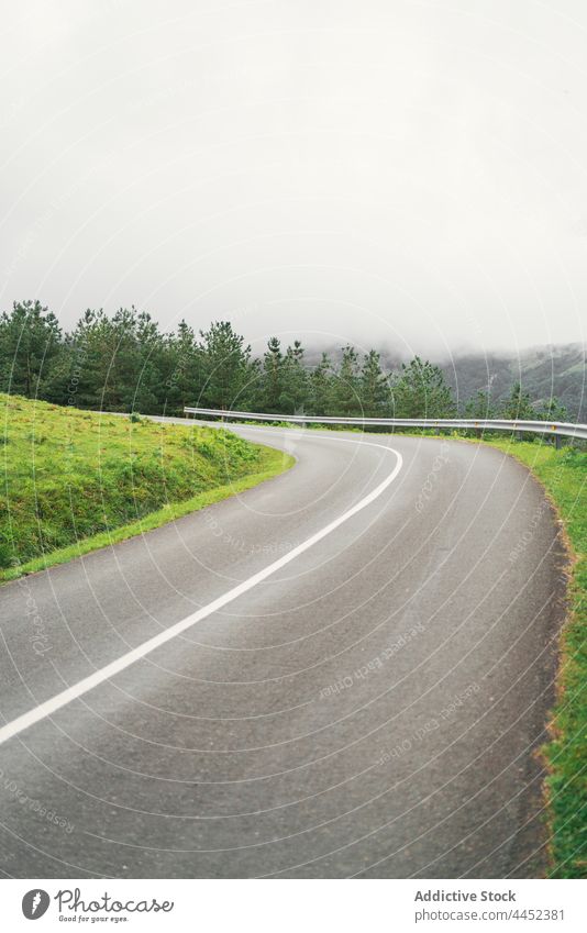 Curved road against mountain in foggy weather route direction sky tree nature highland countryside asphalt lane roadway vegetate curve fence scenic mist growth
