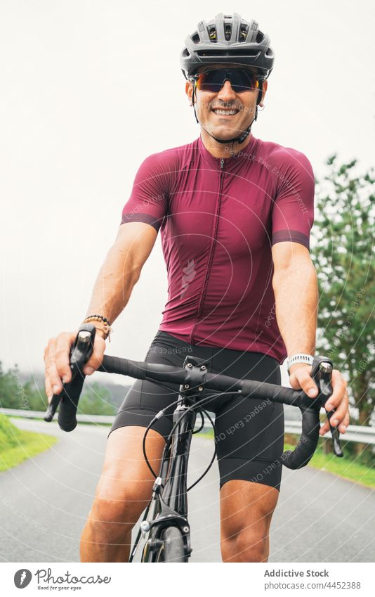 Smiling bicyclist in protective helmet on bike on roadway smile sport cycling sunglasses man countryside portrait creative design contemporary asphalt sit