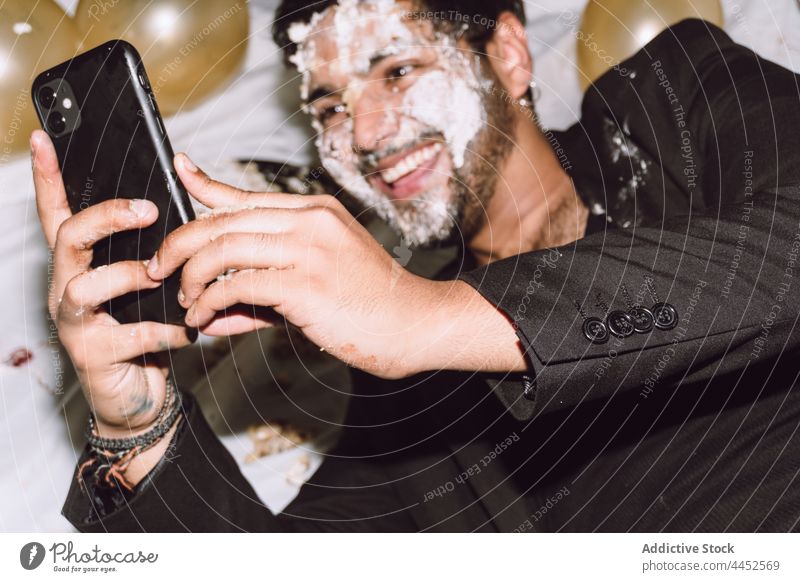 Smiling man with cake on face taking selfie smartphone smash balloon using party fun birthday male watch positive device happy take photo self portrait gadget