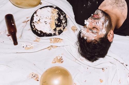 Drunk man lying on messy cloth with smashed cake drunk alcohol party sleep birthday tired male holiday wasted drink dessert rest balloon sweet table eyes closed