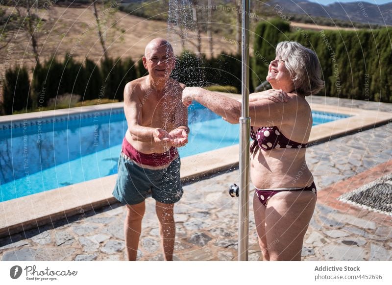 Smiling senior couple having shower on poolside wash refresh enjoy water pleasure husband man woman wife together positive sunlight shirtless wrinkle