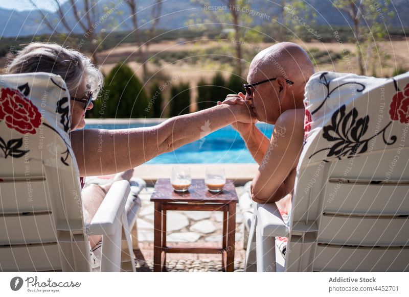 Man kissing hand of wife while chilling on poolside couple love senior lounger gentle romantic bonding woman husband pensioner summer tender close relation