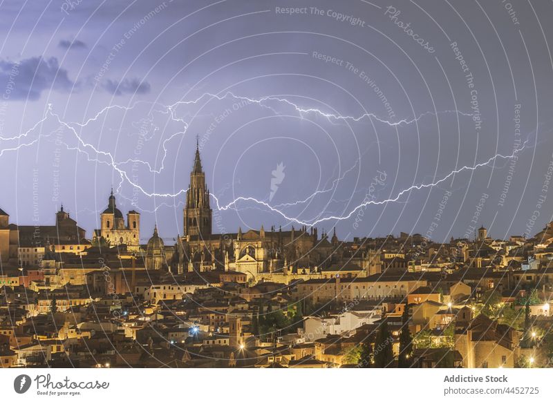 Stormy sky over city with tall aged tower in night time lightning thunderstorm cityscape cloudy building urban toledo spain illuminate electric glow atmosphere