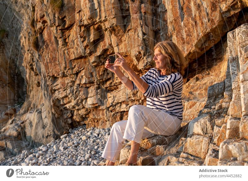 Woman taking photo on smartphone against cliff woman take photo memory moment coast nature highland using gadget device cellphone shore pebble free time