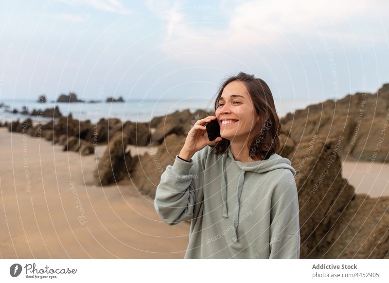 Cheerful woman talking on smartphone on rocky coast cheerful seacoast nature spare time cloudy using gadget sky seashore smile landscape highland ocean