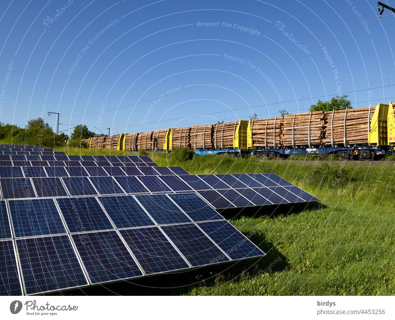 Open land - photovoltaic plant . In the background a freight train loaded with tree trunks passes by photovoltaics Ground-mounted photovoltaic system