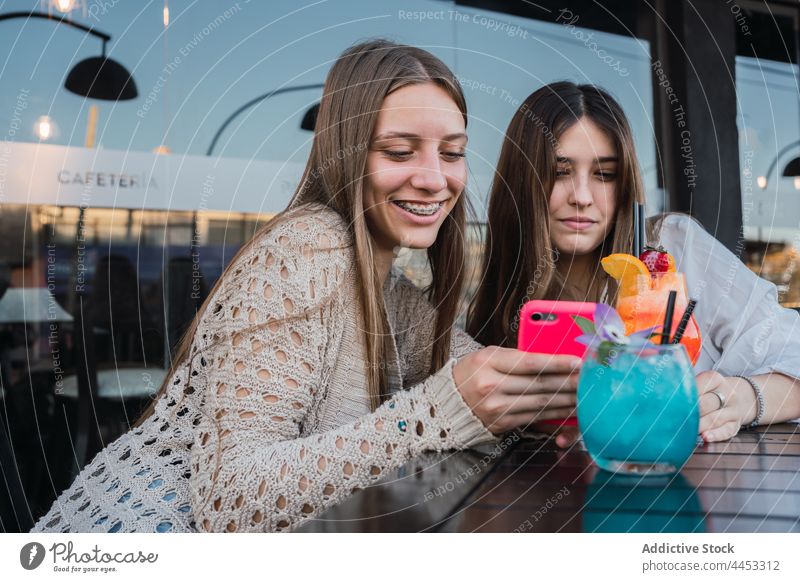 Girlfriends with cocktails browsing on smartphone in street cafeteria girlfriend memory moment spend time using gadget urban best friend smile touch hair gather