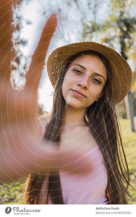 Teen showing hand in summer park teen frame photo perspective picture smile brace sincere portrait friendly straw hat garment photography gaze symbol