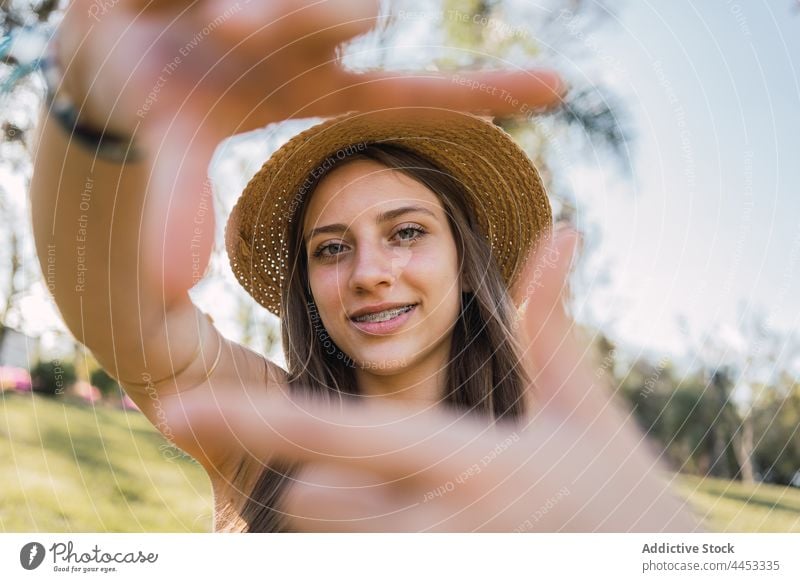 Teen showing frame gesture in summer park teen photo perspective picture smile brace sincere portrait friendly straw hat garment photography gaze symbol