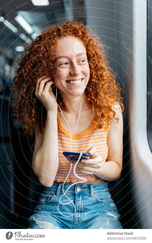 Smiling passenger with smartphone listening to music from earphones candid commute woman train using gadget travel internet smile content cheerful enjoy song