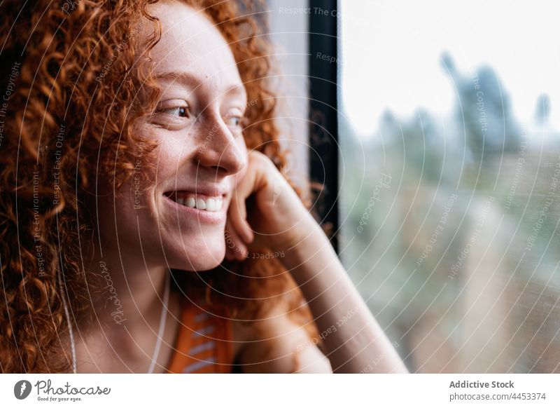 Smiling passenger looking out of window on train look out listen music earphones smile woman using gadget device song melody audio sound lean on hand admire